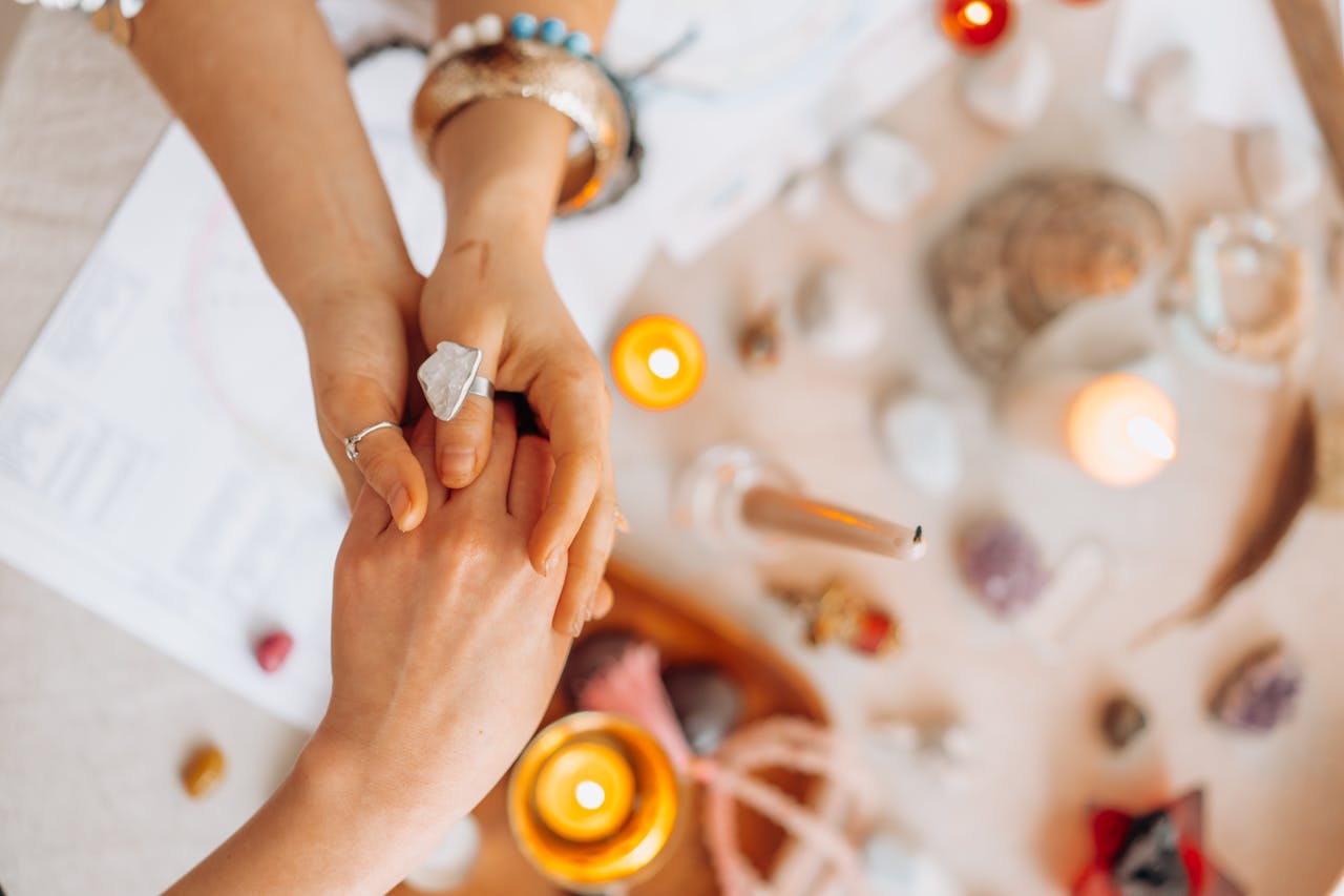 Hands exchanging energy with crystals and candles on a mystic table setting.